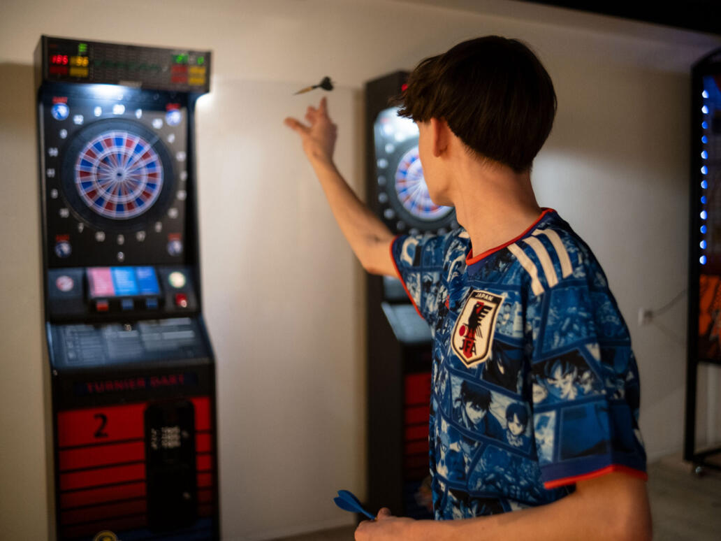 Person wirft einen Dartpfeil auf eine elektronische Dartscheibe im Spielbereich des Säntisparks.