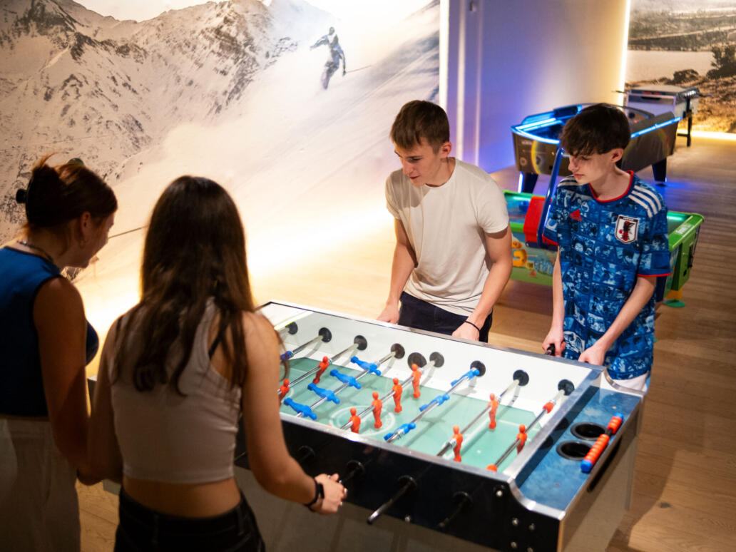 Vier Personen spielen Tischfussball im Freizeitbereich des Säntisparks, weitere Spielgeräte stehen im Hintergrund.